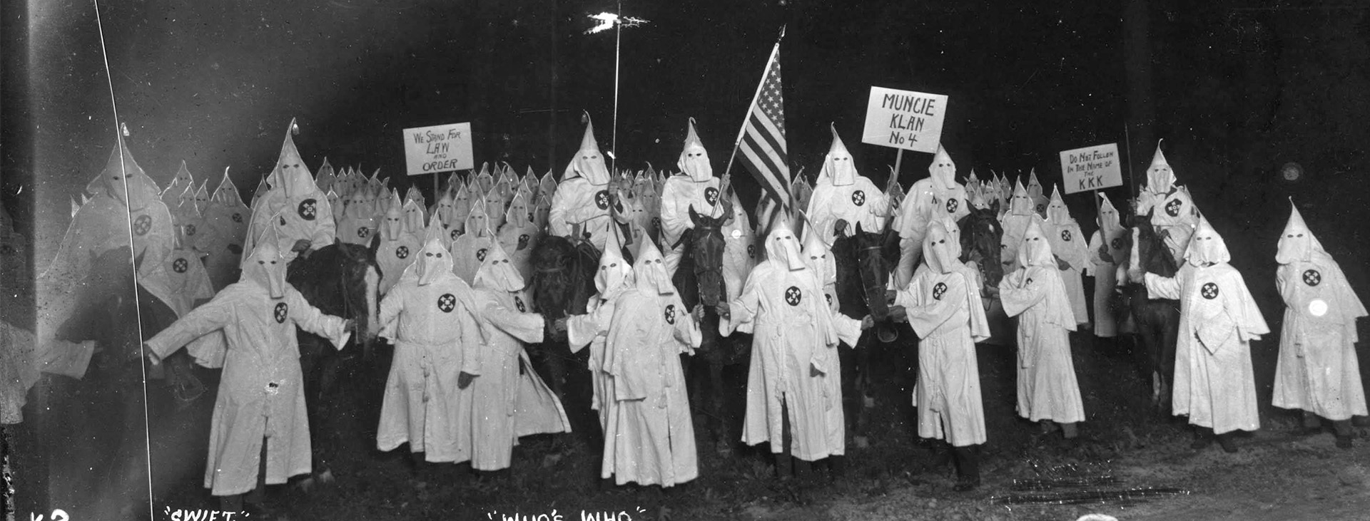 Robed and hooded Klan members hold signs and the American flag. Signs say: “We stand for law and order;” “Muncie Klan No. 4;” “Do not follow in the name of the KKK.” Written on image: “Who's who” and “K-2.”