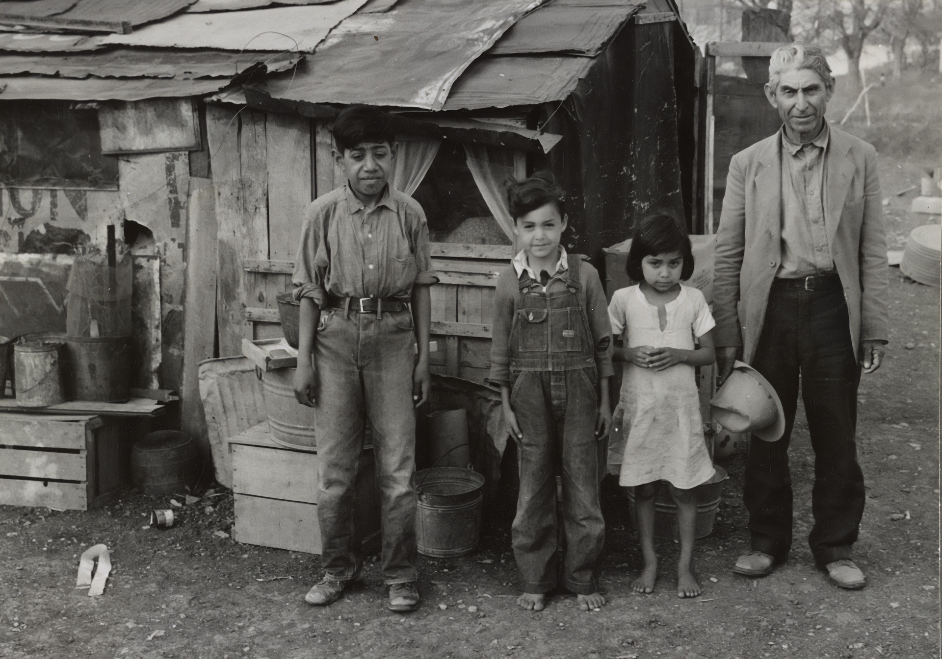 Senor Vigues and three of his five children outside of their homemade shack home opposite Santa Rita Courts, an early segregated public housing project. Located in Austin, Texas the project was one of the first to be completed under the Housing Act of 1937 and was constructed for Mexican American families.
